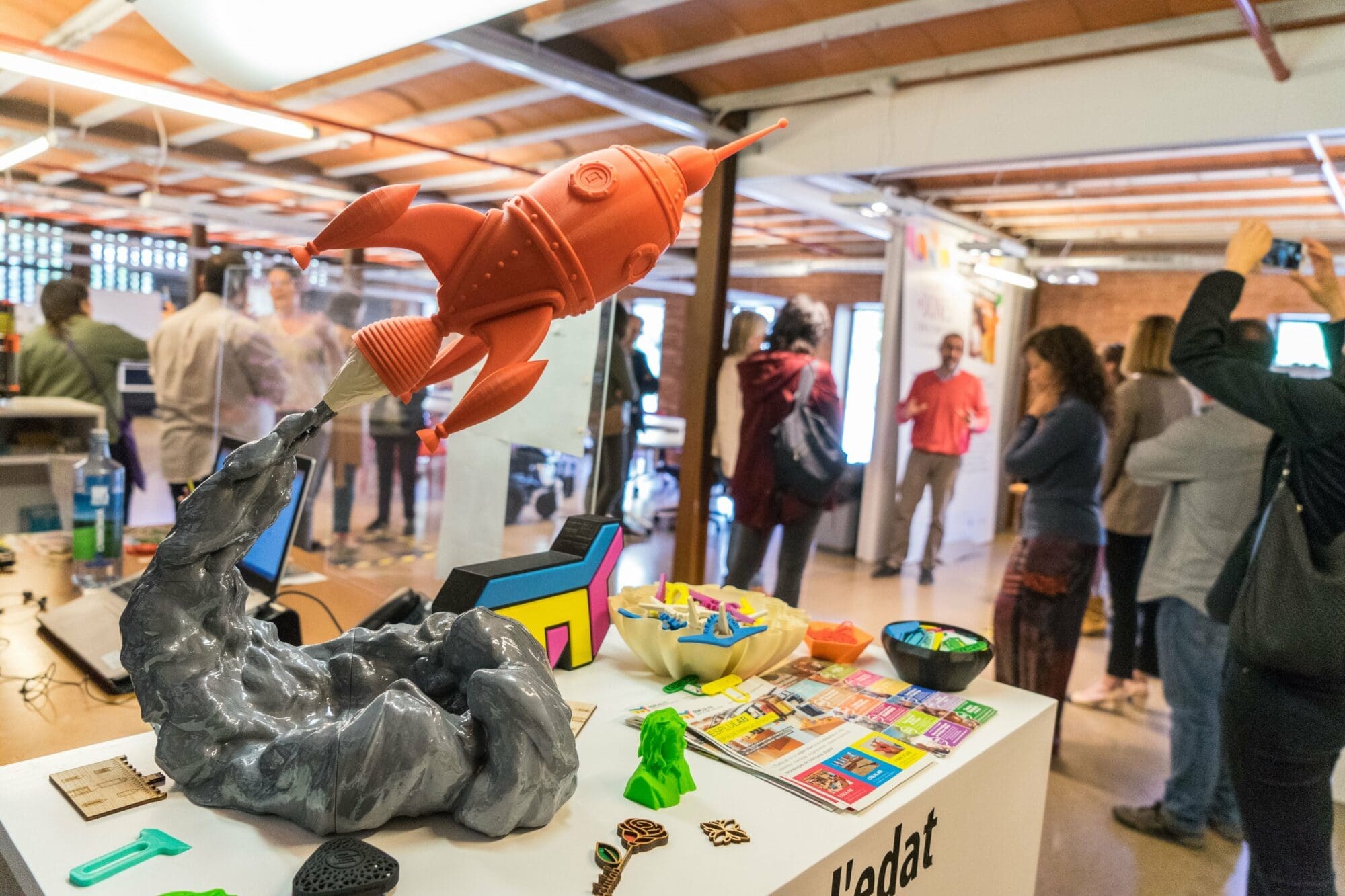 Piezas hechas en el EspluLab en formato 3D, de fondo hay personas hablando en este espacio de fabricación digital