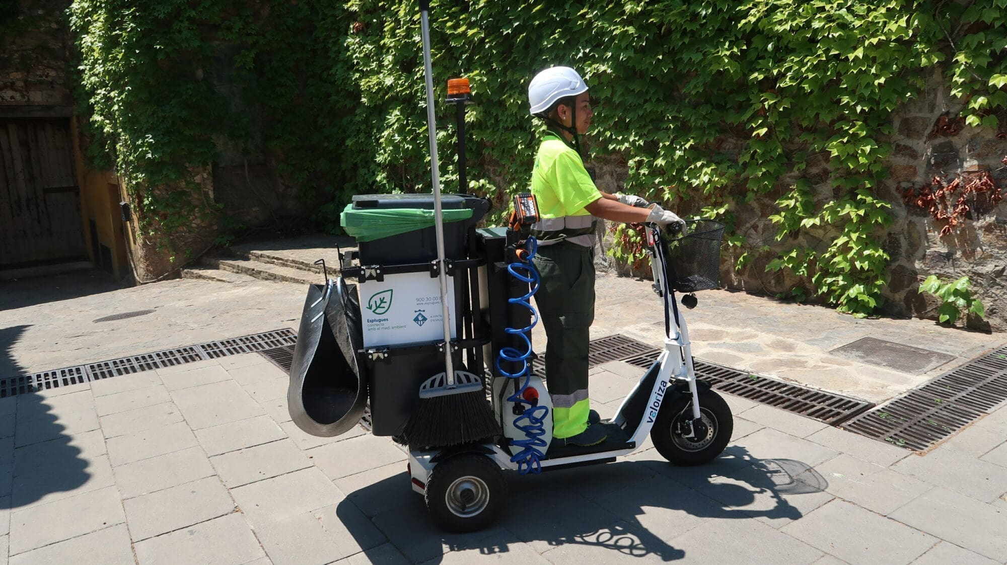 Persona sobre un patinet elèctric que transporta material de neteja.