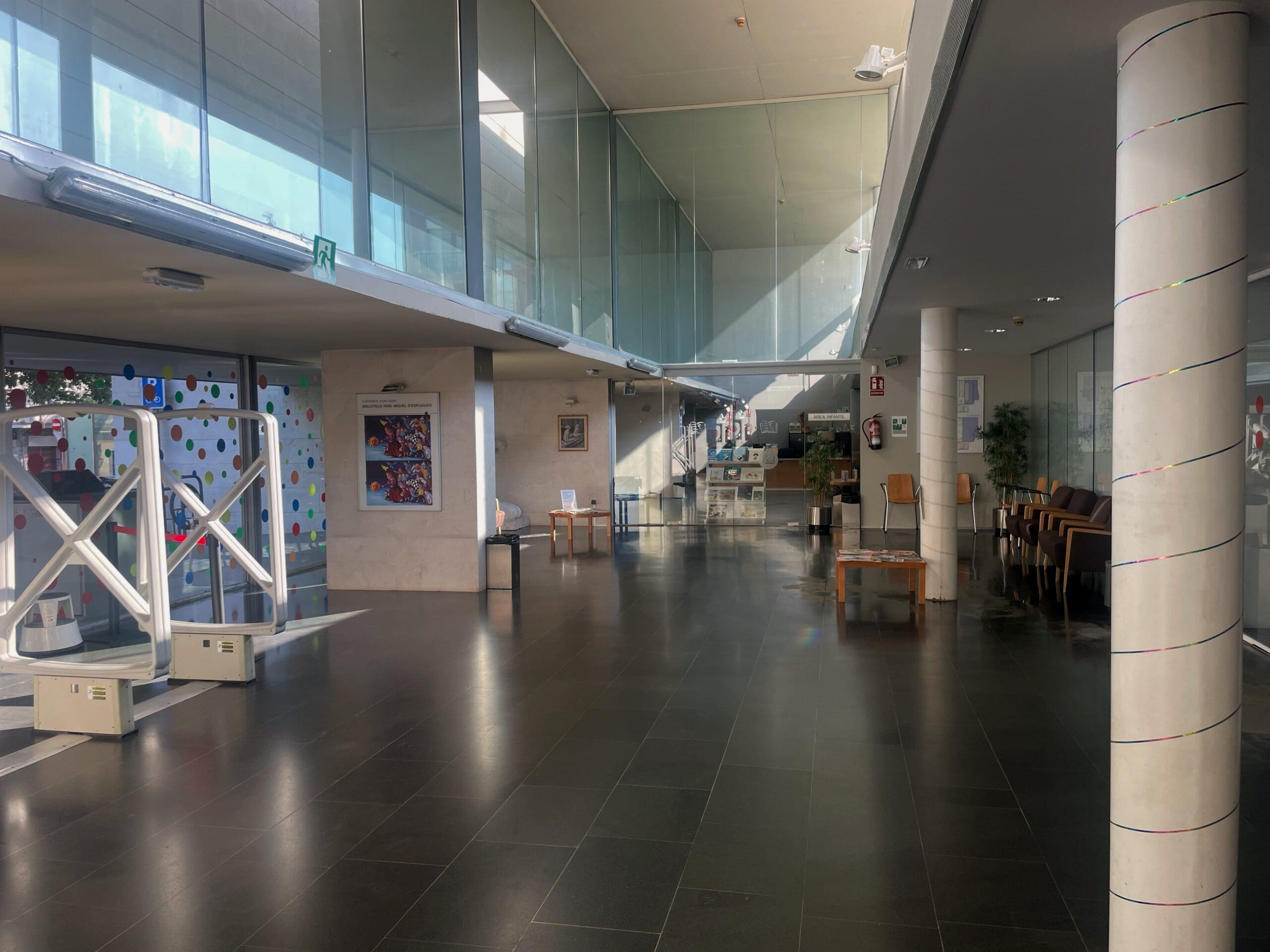 Interior i vista de l'entrada del vestíbul de la Biblioteca Pare Miquel d'Esplugues amb seients i ventilació per a refugi climàtic